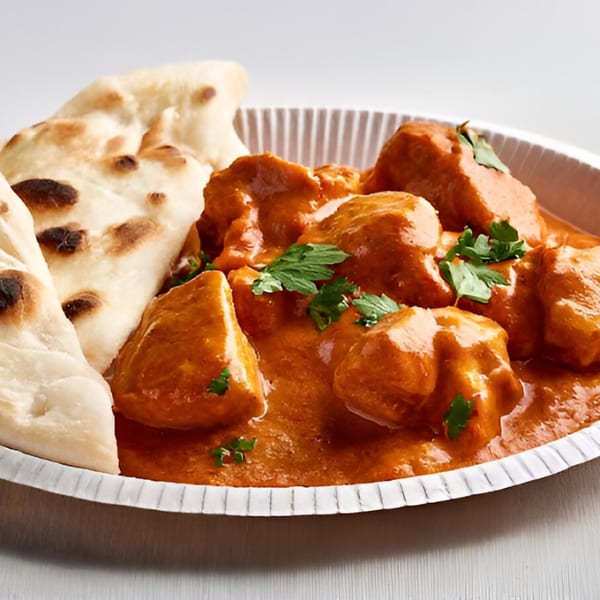 Indian butter chicken with cilantro and naan bread in a white paper bowl.