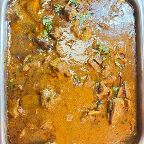 Close-up of a large tray of Indian curry with meat pieces and cilantro garnish.