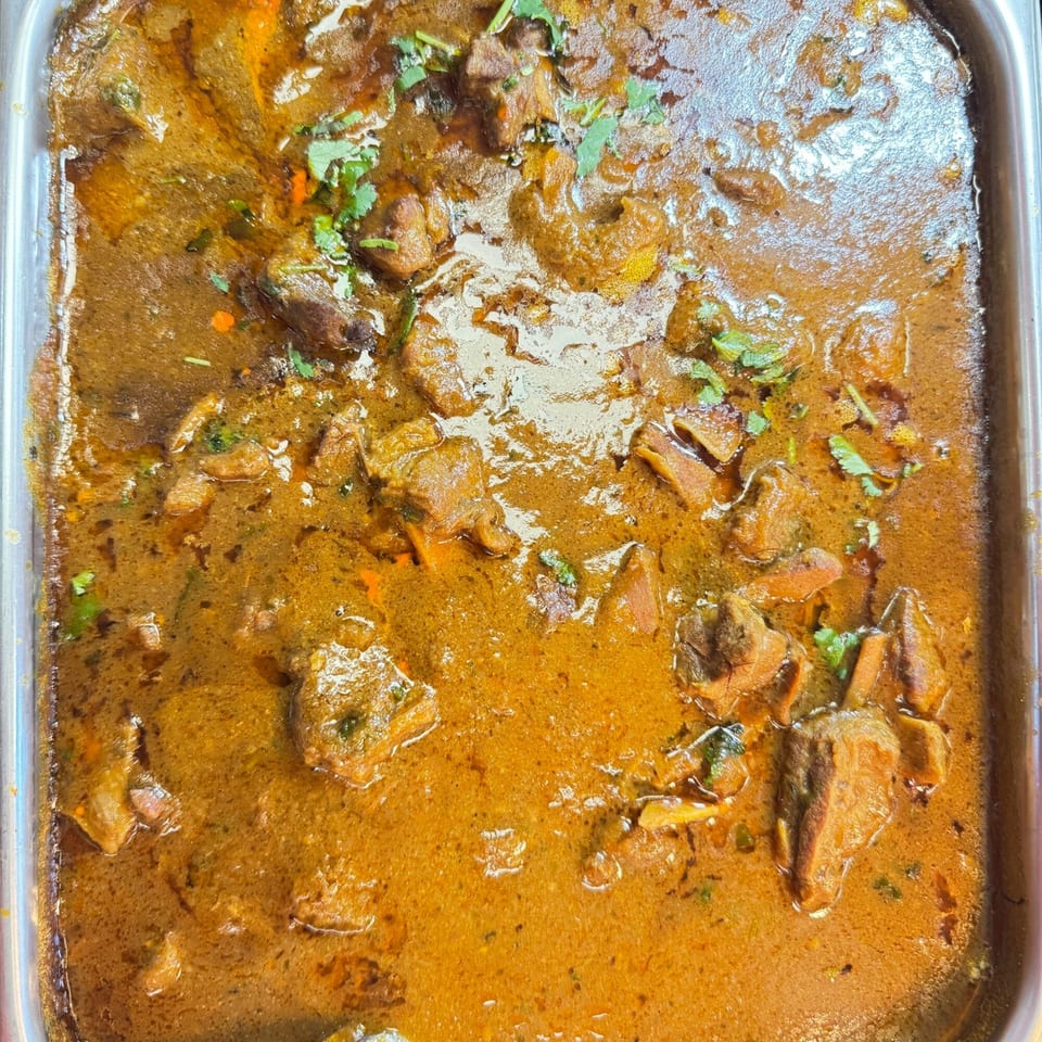 Close-up of a large tray of Indian curry with meat pieces and cilantro garnish.