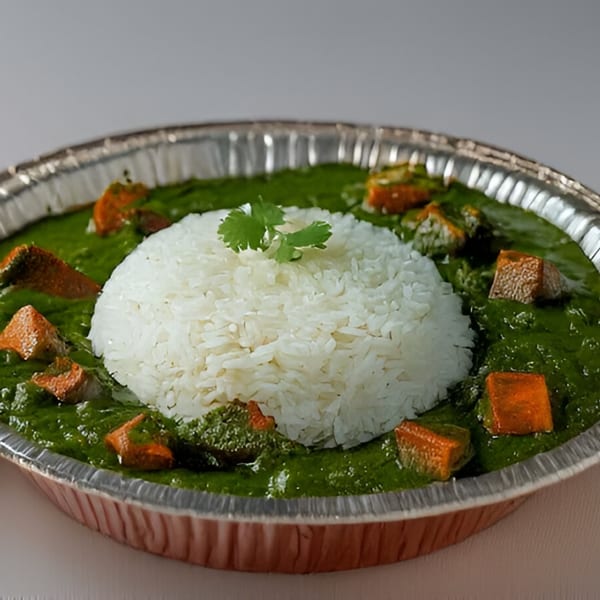 Palak Paneer with a mound of white rice and cilantro in a foil takeout container.