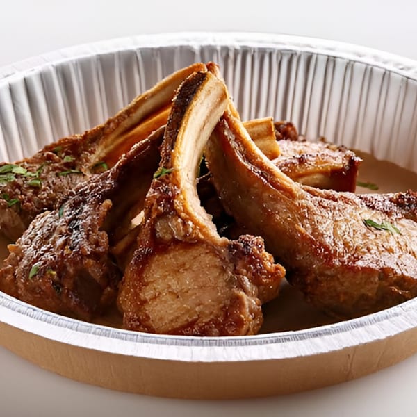 Indian lamb chops, seasoned and cooked, served in a round foil takeout container.